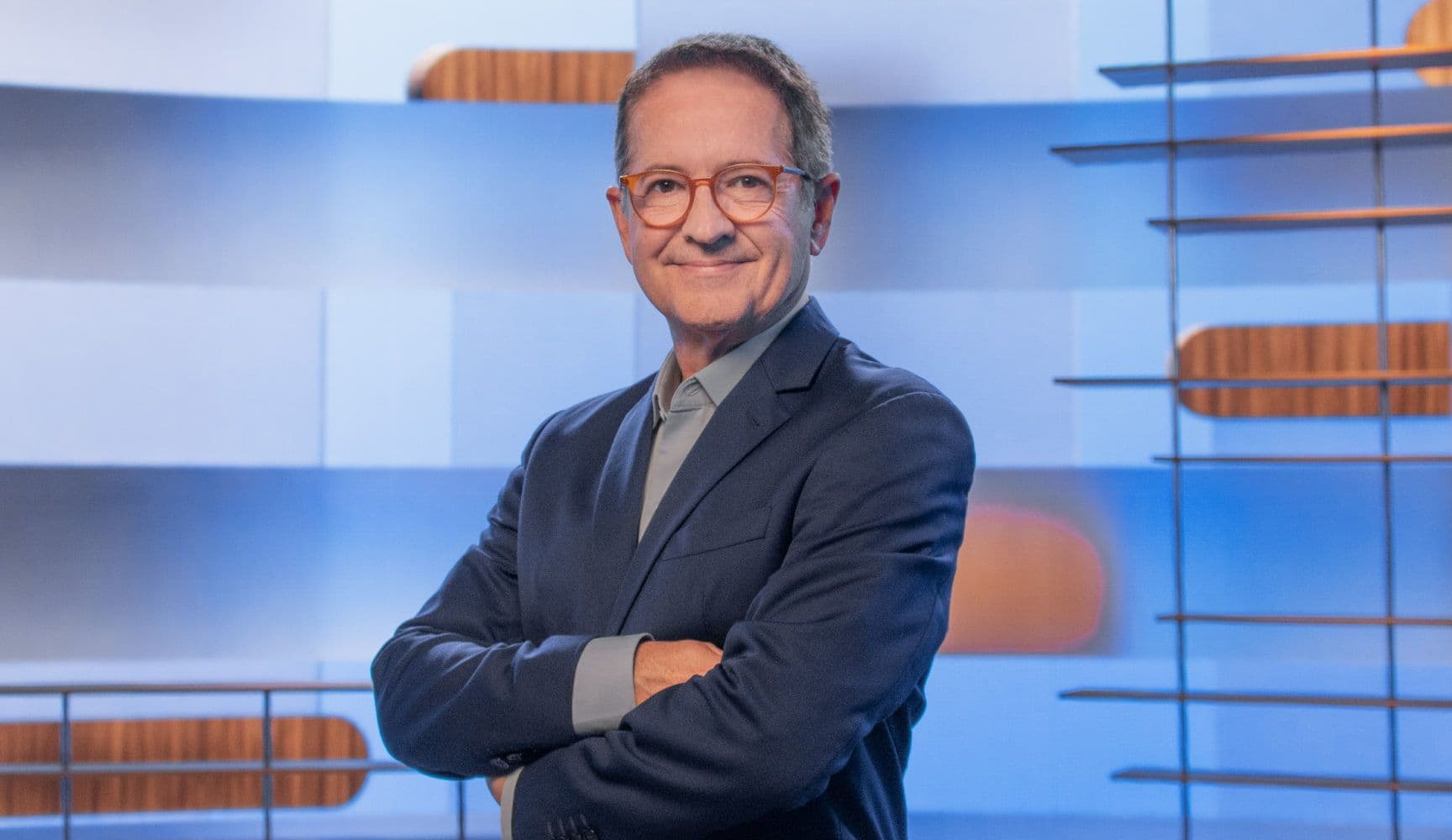 Foto de um homem em pé, sorrindo com os braços cruzados