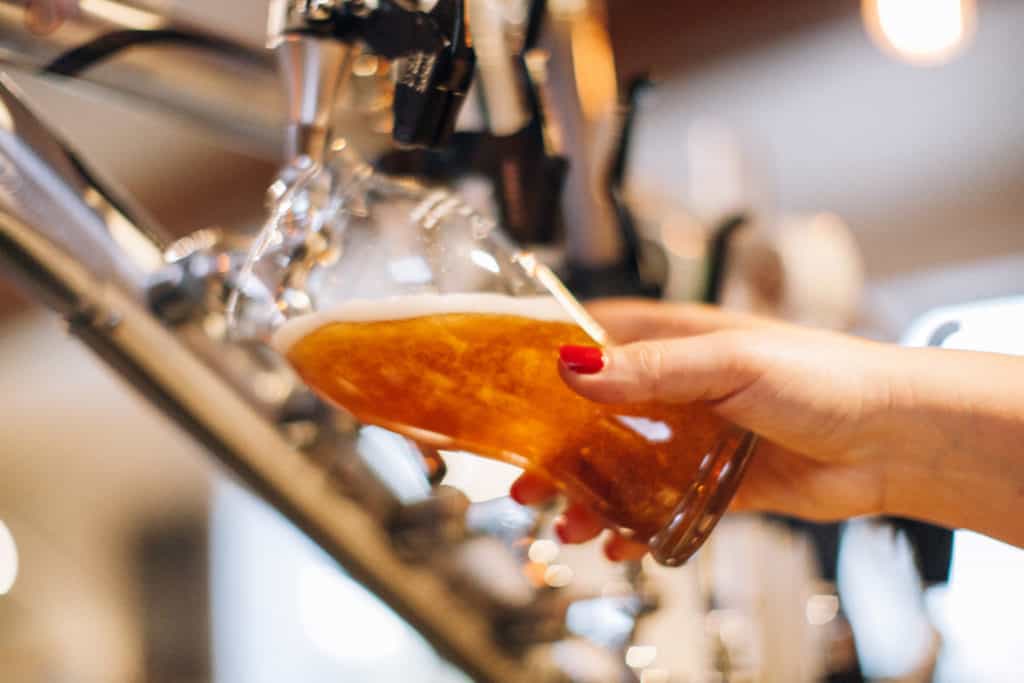 Detalhe de pessoa tirando chopp em torneira representando as cervejarias em Curitiba