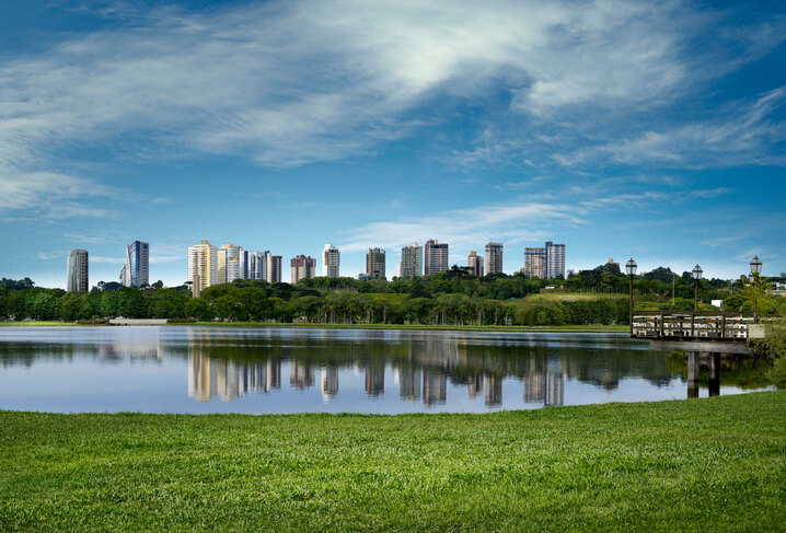 Foto que ilustra matéria sobre os bairros mais seguros de Curitiba mostra um lago do Parque Barigui com prédios altos ao fundo.