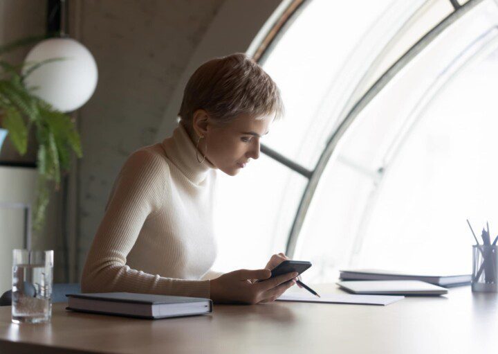 Mulher com celular na mão analisa documentos representando a verificação de seu contrato de aluguel de imóvel