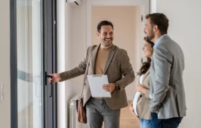 Fotografia de um casal cumprimentando um corretor imobiliário.