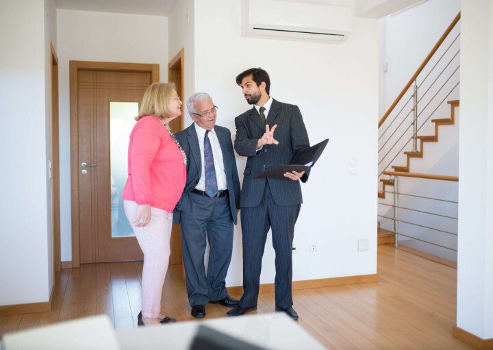 Foto que ilustra matéria sobre matrícula de imóvel, com um corretor explicando os procedimentos para um casal de um homem e uma mulher idosos.