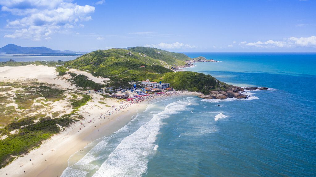 Imagem de uma praia em Florianópolis, mostrando o mar azul, a faixa de areia e a vegetação de uma das melhores cidades para morar no Brasil