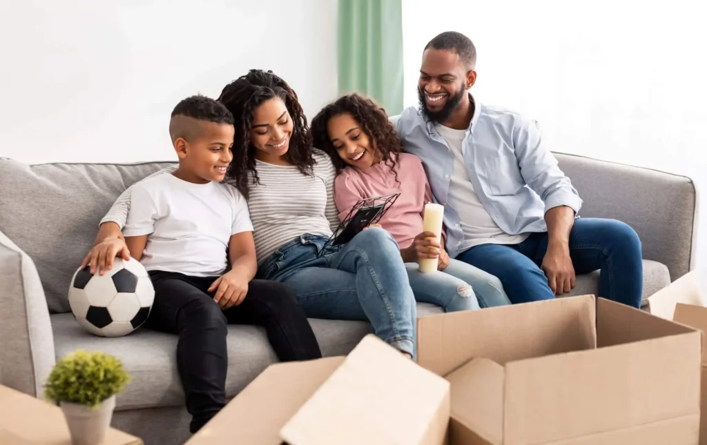 Imagem de uma família composta por um homem, uma mulher e duas crianças sentados no sofá de casa para ilustrar matéria sobre qual é o melhor bairro para morar em SP