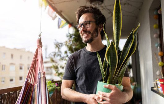 Em foto que ilustra um teste de personalidades sobre plantas em casa, um homem segura um vaso com uma planta da espécie espada de São Jorge.