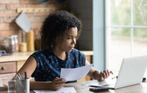 Mulher negra revisa documentos em frente ao computador.