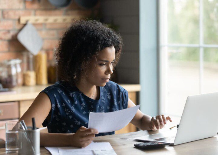 Mulher negra revisa documentos em frente ao computador.