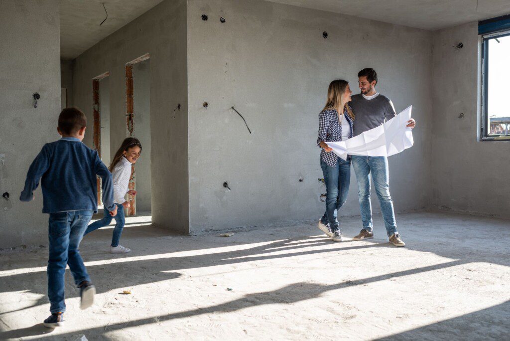 Família feliz analisando planos em seu novo apartamento, em reforma. Imagem disponível em Getty Images.