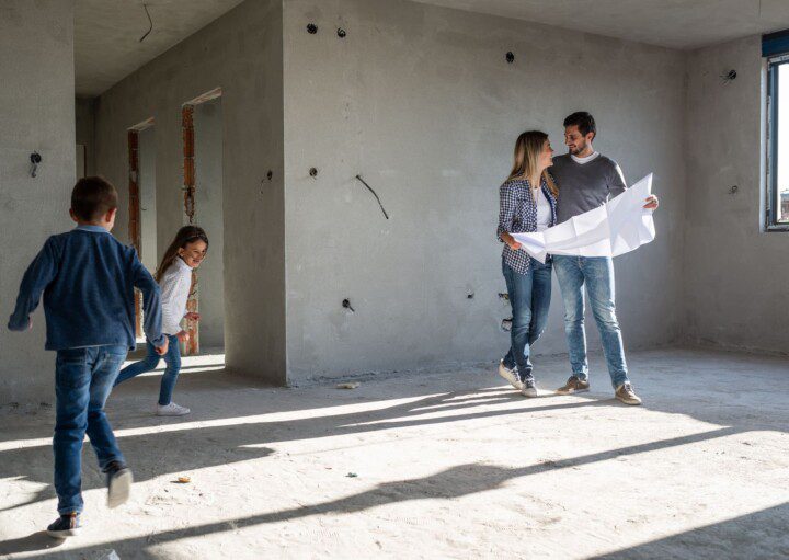 Família feliz analisando planos em seu novo apartamento, em reforma. Imagem disponível em Getty Images.