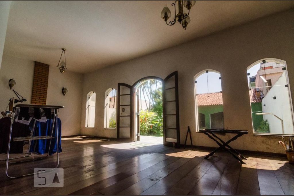 Uma sala, com vista para uma porta dupla aberta e amplas janelas mostrando uma área com árvores e um ambiente verde ao fundo