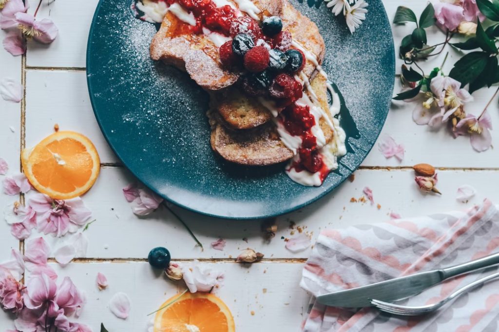 prato com um tradicional café-da-manhã francês, torrada com geleia e frutas, decorado com flores e laranjas, simulando uma das várias opções gastronômicas em Cerqueira César 