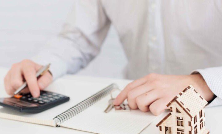 Mãos segurando caneta e calculadora sobre um caderno para fazer o inventário de imóvel