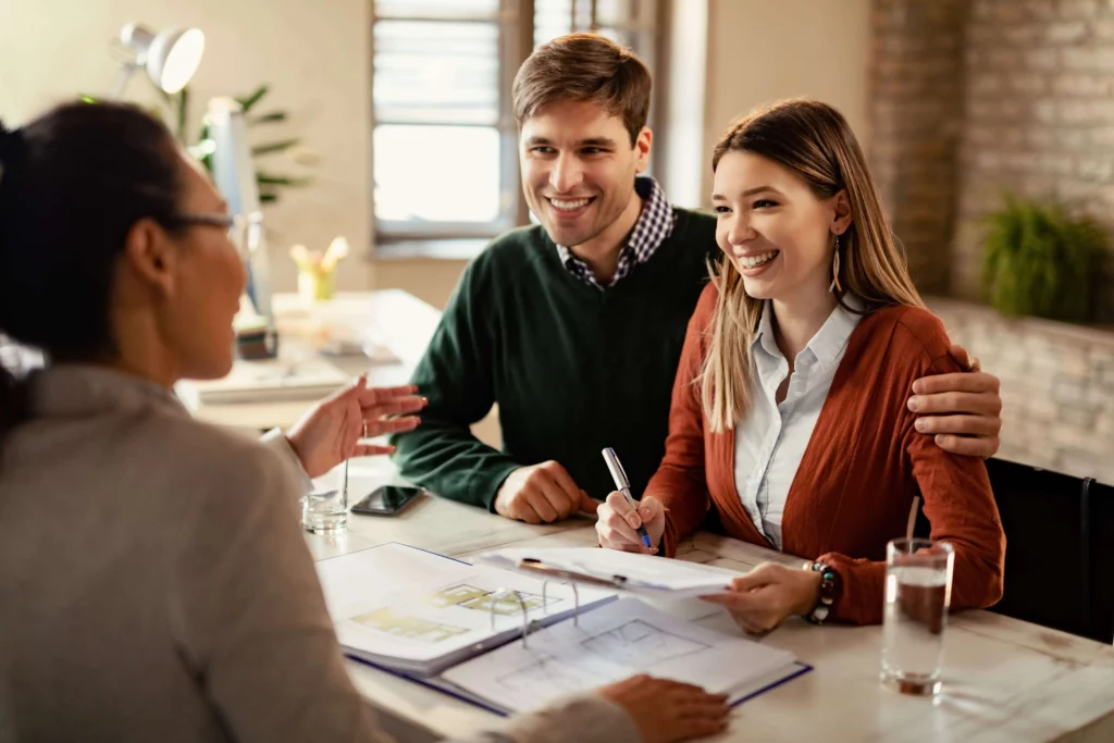 Imagem de um casal assinando um documento na frente de uma agente imobiliária para ilustrar matéria sobre como financiar um apartamento 