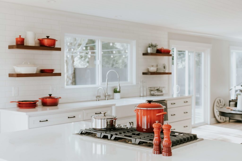 Cozinha toda na cor branca, decorada com panelas laranjas. Várias prateleiras dispõem da decoração