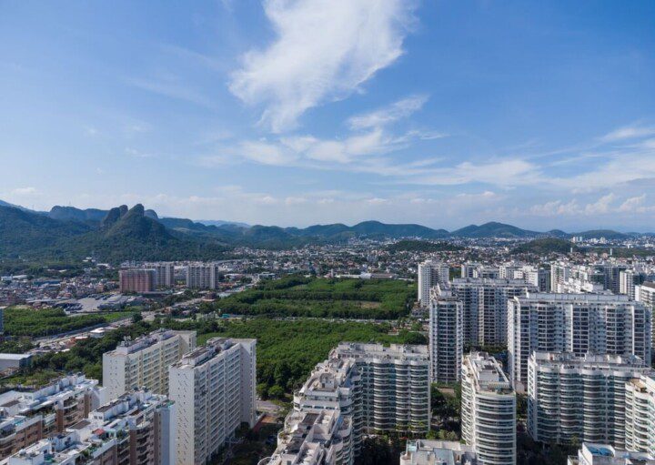 Foto que ilustra matéria sobre a Zona Oeste do RJ mostra uma vista aérea de Jacarepaguá, com grandes condomínios de prédios residenciais em primeiro plano e montanhas ao fundo.