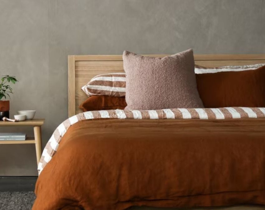 quarto simples bem decorado, com uma cama de casal com roupa de cama em tons marrons e uma mesa de cabeceira ao lado