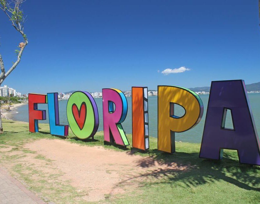 Foto que ilustra matéria sobre o que fazer em Florianópolis mostra em detalhes um letreiro com a palavra “Floripa” escrita em letras coloridas à beira de uma das praias da cidade.