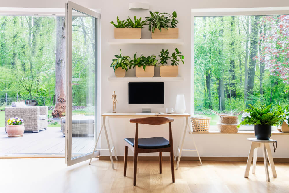 Foto de uma sala de estar. Nela há 3 pessoas: uma mulher usando o notebook no sofá, um homem sentado diante de uma mesa usando um notebook e uma criança próxima ao homem brincando. 