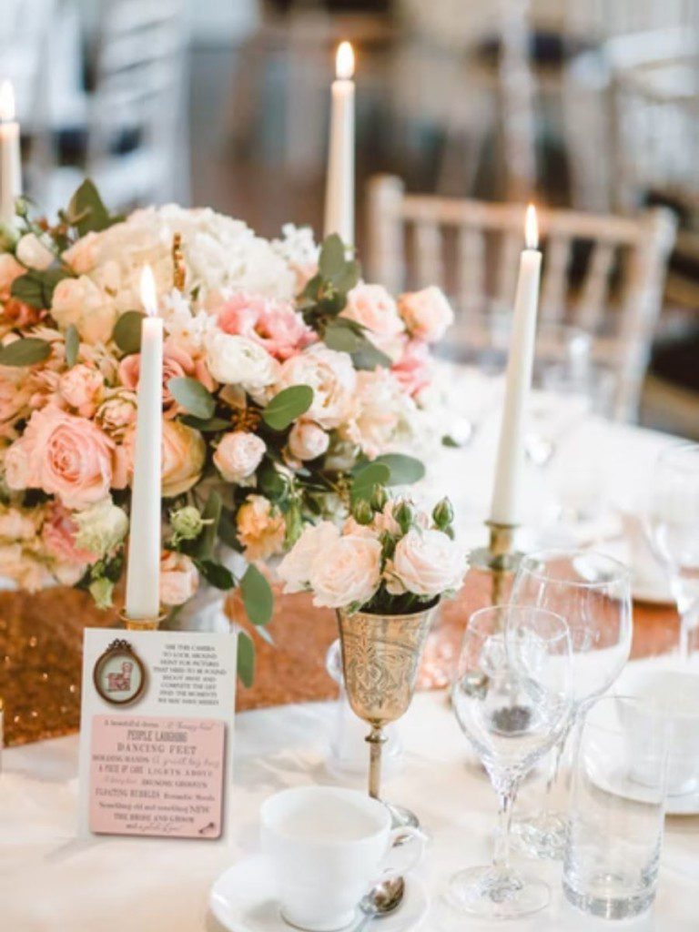 A imagem mostra a decoração de chá de cozinha com tema definido, mesa posta com flores rosas, velas, pratarias e cristais finos.