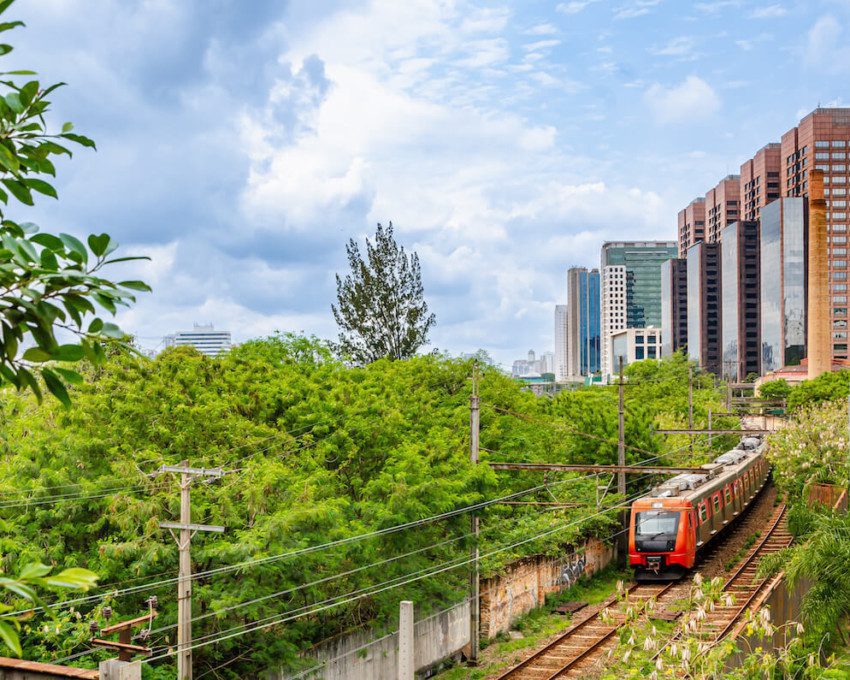 Foto que ilustra matéria sobre mapa trem sp mostra uma linha ferroviária com um trem em movimento com grama e árvores verdes dos lados