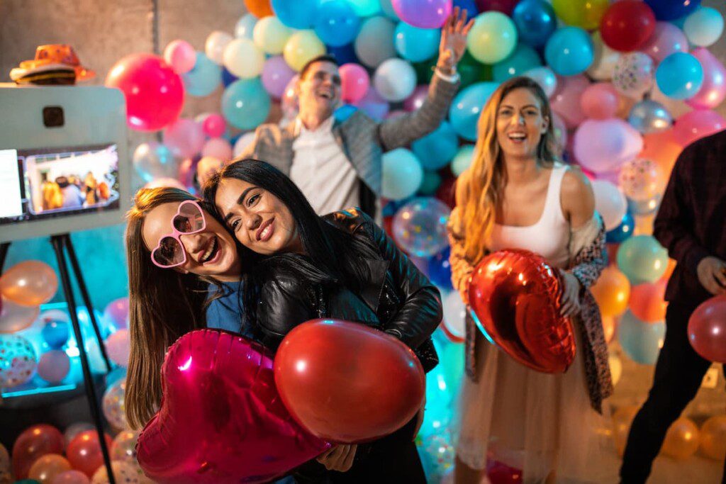 Na foto é possível ver quatro pessoas segurando balões em forma de coração em uma festa.