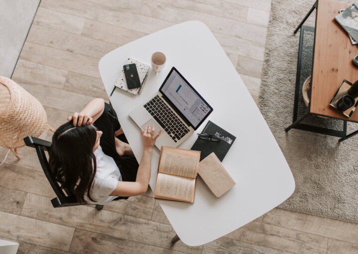 Foto que ilustra matéria sobre melhor investimento para reserva de emergência mostra uma mulher sentada à mesa mexendo no computador e estudando gráficos.