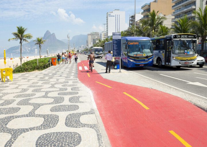 Foto que ilustra matéria sobre o custo de vida no Rio de Janeiro mostra um pedaço do calçadão da Avenida Vieira Souto, em Ipanema à esquerda, com uma pista de ciclovia ao centro e a faixa de tráfego à direita, onde aparecem dois ônibus.