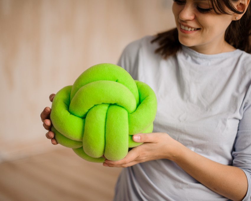 Imagem de uma mulher segurando uma almofada de nó verde.