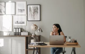 Foto que ilustra matéria sobre como se proteger da inflação com investimento em imóveis mostra uma mulher sentada em frente a um notebook com uma caneta na mão séria e pensativa