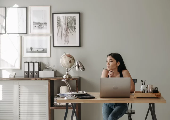 Foto que ilustra matéria sobre como se proteger da inflação com investimento em imóveis mostra uma mulher sentada em frente a um notebook com uma caneta na mão séria e pensativa