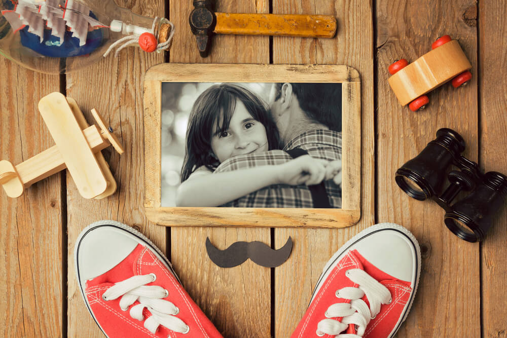 Foto que ilustra matéria sobre decoração para dia dos pais mostra um porta-retrato com uma foto em preto e branco de uma menina sorrindo no colo do pai.