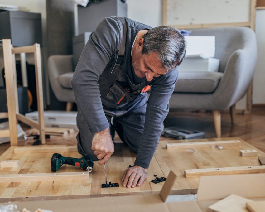 Imagem de um senhor montando uma mesa de madeira.