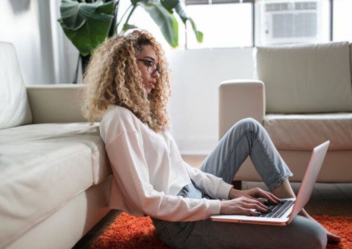 mulher sentada no chão, encostada em um sofá, com o notebook no colo, lendo sobre o que é DIRF