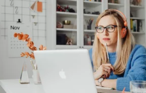 Foto que ilustra matéria sobre imóvel comercial ou residencial mostra uma mulher sentada em frente ao computador com óculos e fones de ouvido com feição concentrada.