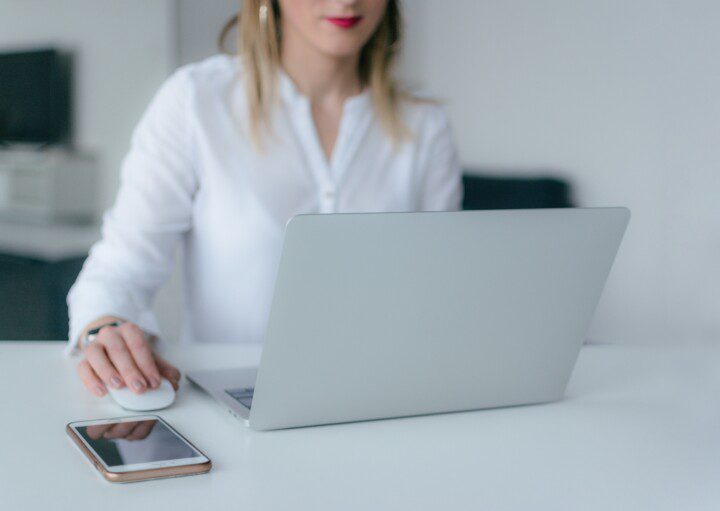 Mulher Usando Laptop Prateado com telefone celular ao lado