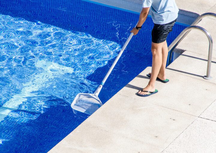 Foto que ilustra matéria sobre como limpar piscina mostra um homem limpando a piscina de casa