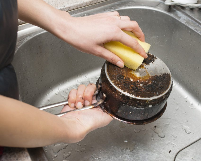 Imagem de uma mulher limpando uma panela queimada com esponja.