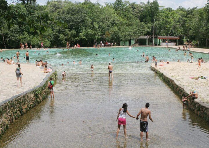 Foto que ilustra matéria sobre parques em Brasília mostra a entrada de uma das piscinas do Parque Nacional de Brasília, repleta de pessoas se banhando e com várias árvores ao fundo.