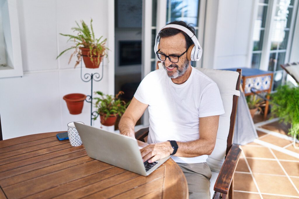 Homem usando laptop e fones de ouvido na varanda. 