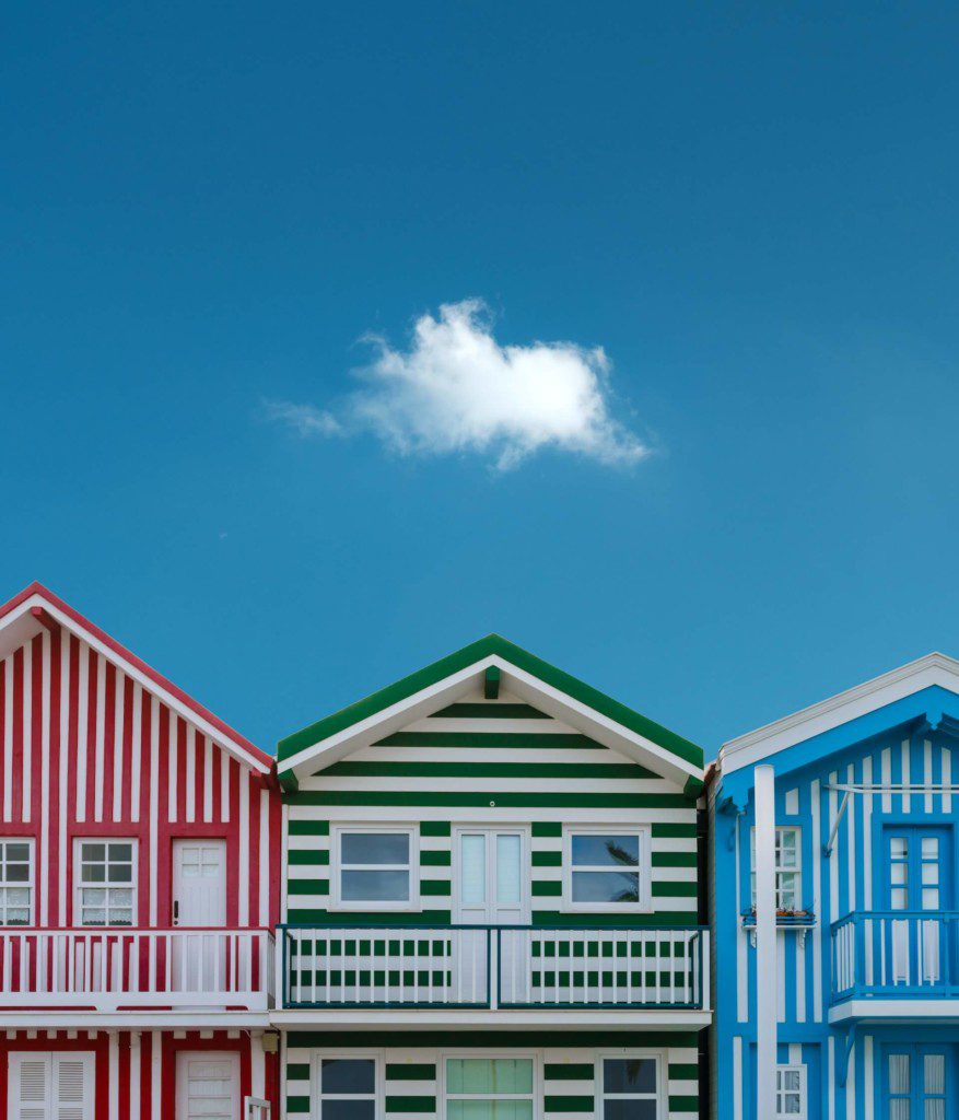 três casas coloridas listradas, lado a lado, uma vermelha, uma verde e uma azul