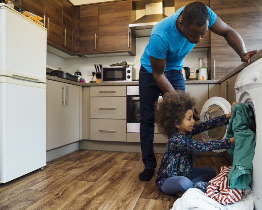 foto que ilustra matéria sobre cozinha com lavanderia mostra um homem e um menino colocando roupa para lavar