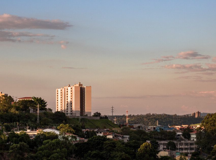 Foto que ilustra matéria sobre onde fica Várzea Paulista mostra uma vista panorâmica da cidade no cair da tarde, com várias árvores e um prédio alto que se destaca no centro da imagem.