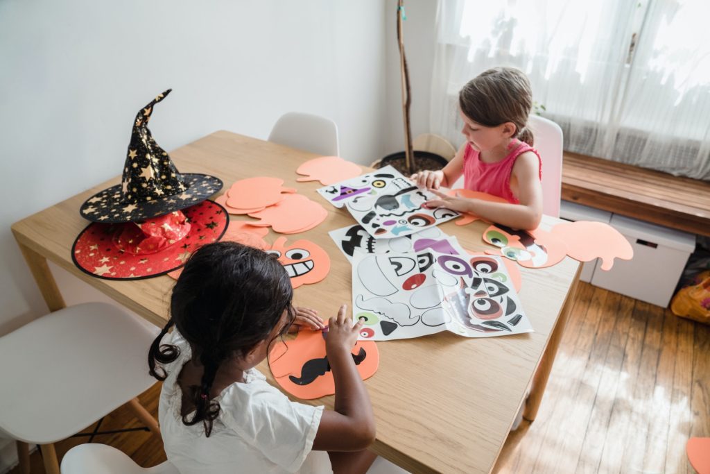 Foto que ilustra matéria sobre decoração de Halloween mostra duas meninas sentadas a uma mesa fazendo carinhas de EVA