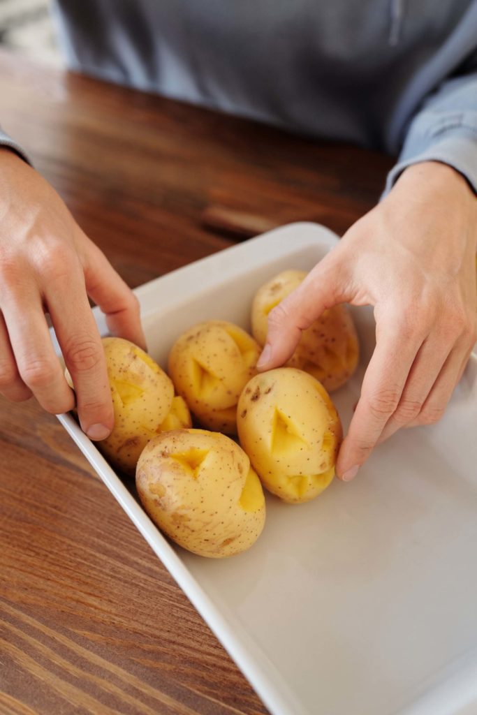 Foto que ilustra matéria sobre decoração de Halloween mostra uma pessoa arrumando batatas com caras assustadoras em uma vasilha