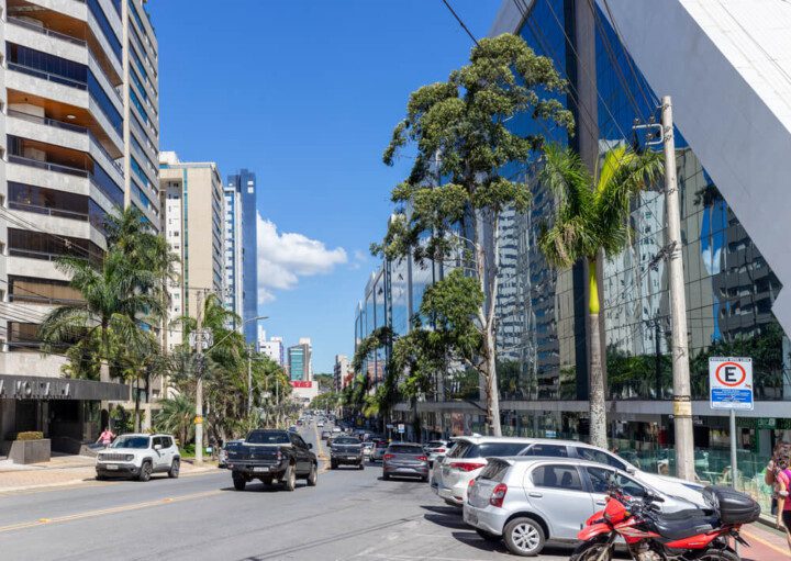 Foto que ilustra matéria sobre o que fazer em Nova Lima mostra uma avenida movimentada do bairro Vila da Serra, onde aparecem prédios grandes e carros.