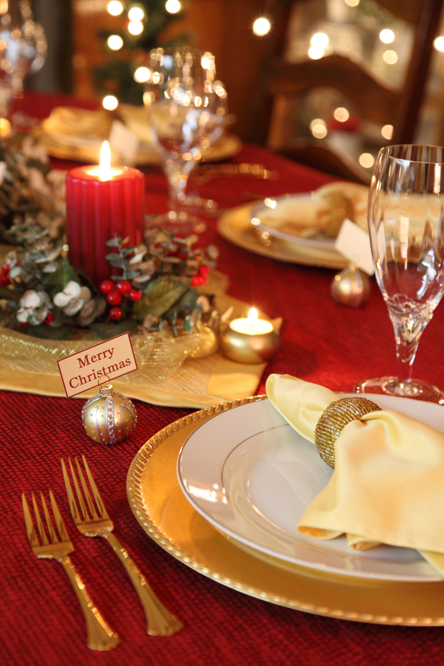 Mesa posta de Natal com talheres dourados, vela vermelha e taças em cristal.