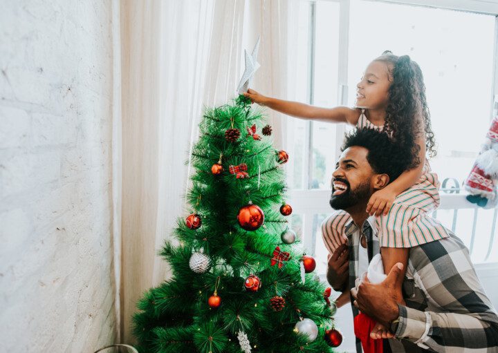 Imagem de pai e filha decorando a árvore de Natal.