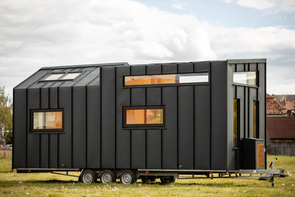 Foto que ilustra matéria sobre tiny house mostra uma estrutura de uma casa construída em cima de um chassi com seis rodas, três de cada lado, e uma estrutura para reboque.