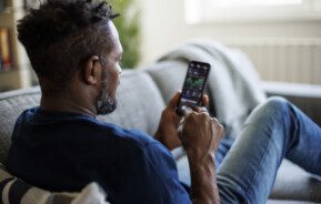 Foto que ilustra matéria sobre como fatores políticos influenciam o mercado imobiliário mostra um homem negro de costas olhando para seus investimentos no celular.