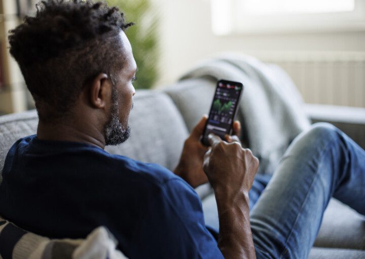 Foto que ilustra matéria sobre como fatores políticos influenciam o mercado imobiliário mostra um homem negro de costas olhando para seus investimentos no celular.